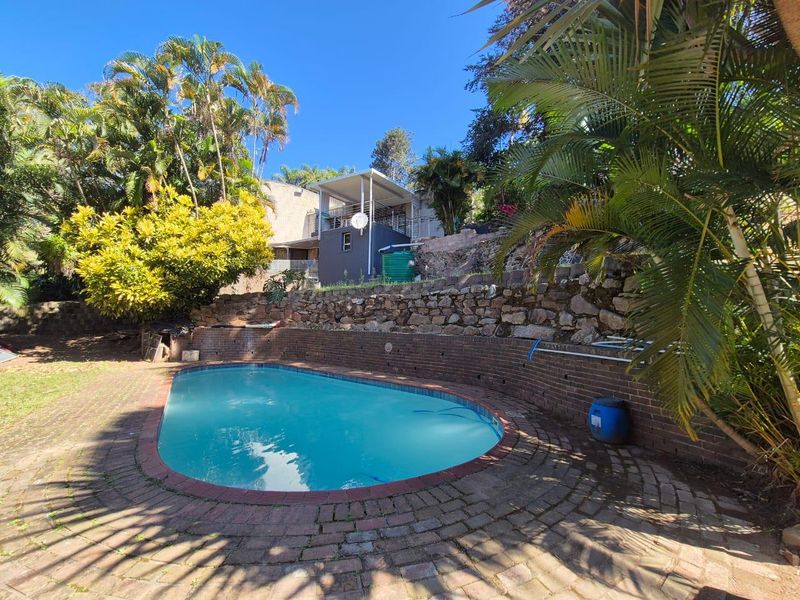 Outdoor pool area featuring a paved surround, stone and brick retaining walls, and established garden landscaping.
