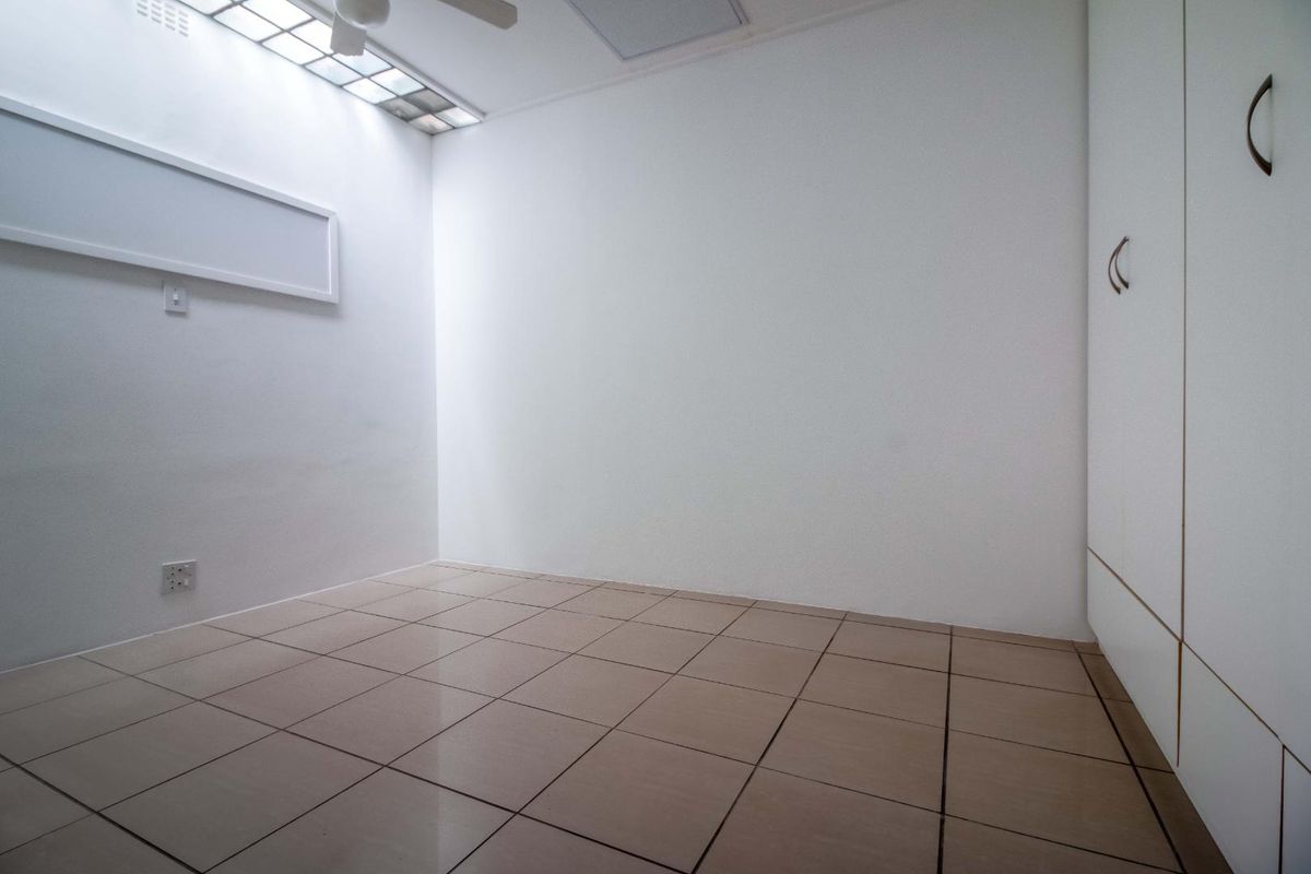 A bright, empty bedroom featuring tiled flooring, built-in cupboards, and a skylight providing natural illumination.