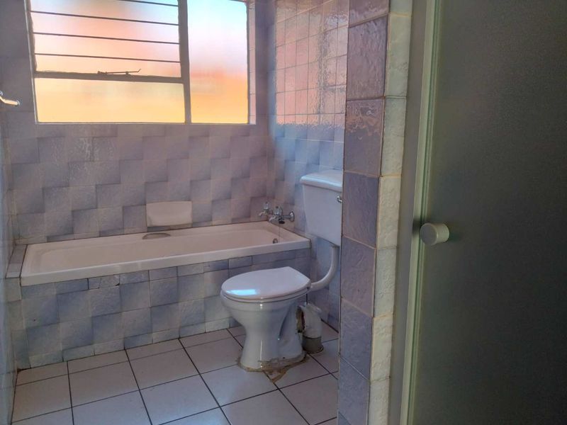 A dated bathroom featuring a built-in bathtub, toilet, and tiled finishes, offering a functional space ready for modernization and cosmetic updates.
