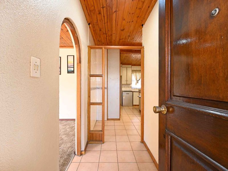 A functional hallway featuring tiled flooring and a timber-clad ceiling, providing access to adjacent living areas and the kitchen.
