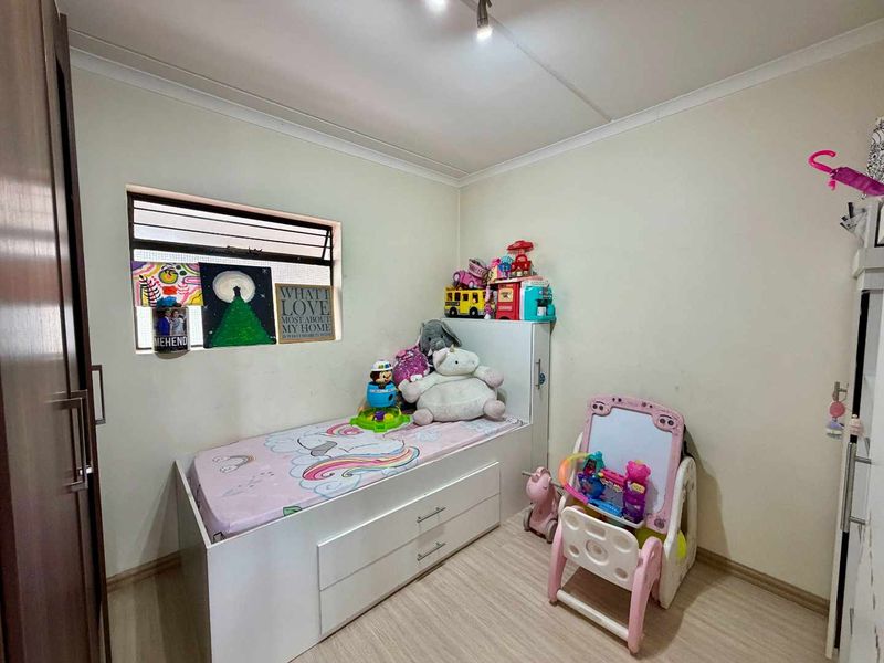 A compact bedroom featuring laminate flooring, a built-in cupboard, and a louvre window, providing a functional space for a child's room.