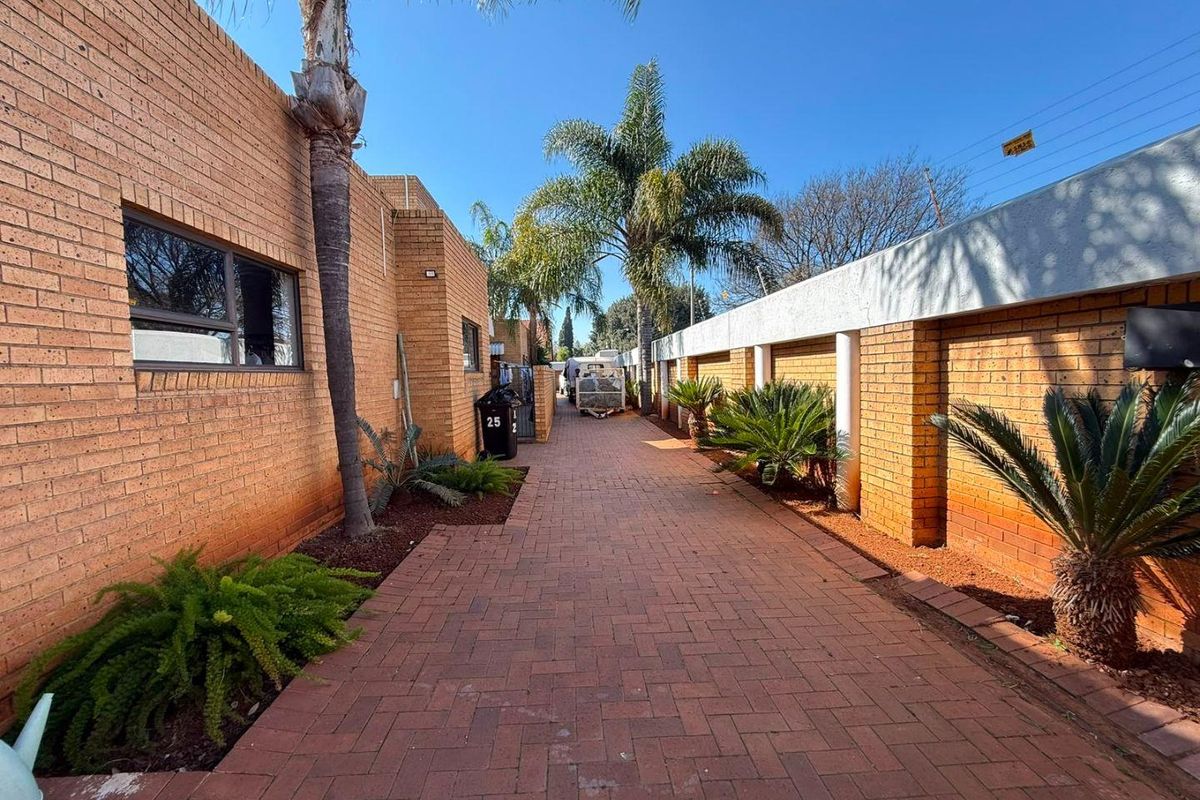 A paved side walkway featuring face brick walls, established palm trees, and a secure boundary wall.