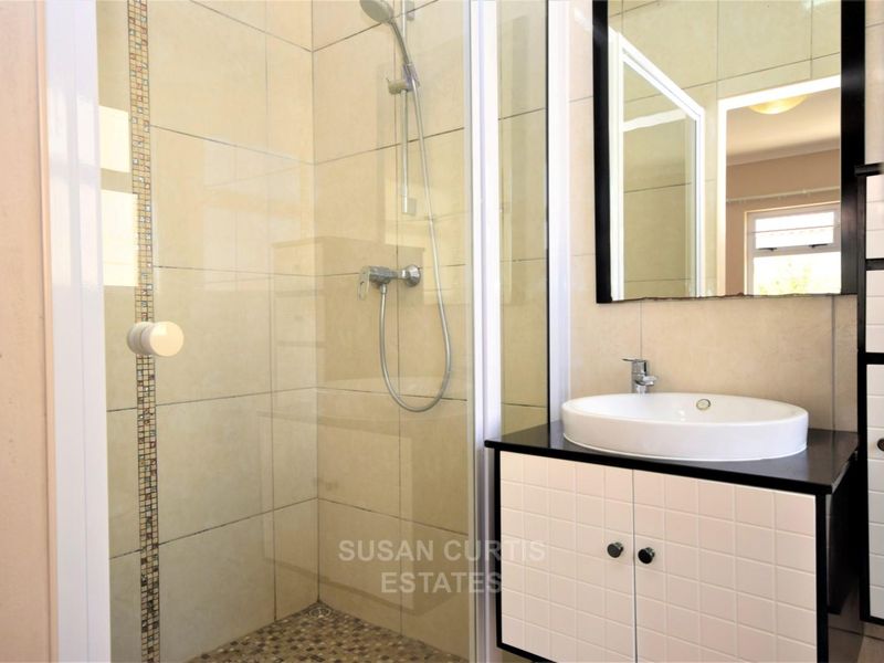 A modern bathroom featuring a glass-enclosed shower with mosaic tile accents, a vessel sink vanity, and neutral wall tiling.