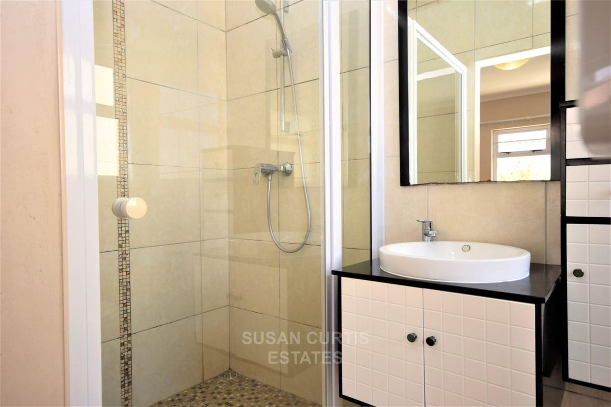 A modern bathroom featuring a glass-enclosed shower with mosaic tile accents, a vessel sink vanity, and neutral wall tiling.