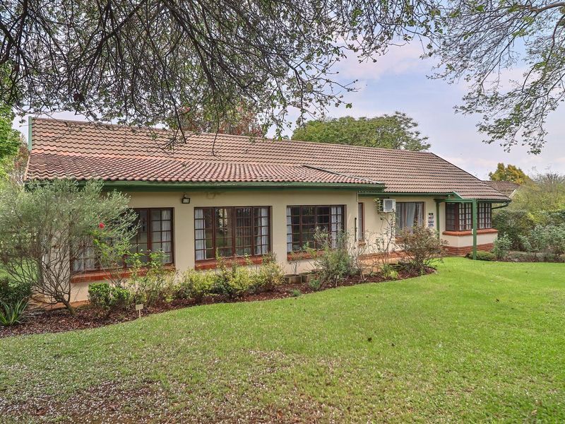 Rear view of a single-story house featuring a tiled roof, brick accents, and established garden surroundings.