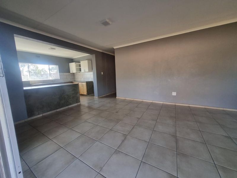 An open-plan living and kitchen area featuring neutral grey walls, tiled flooring, and built-in kitchen cabinetry with a breakfast counter.
