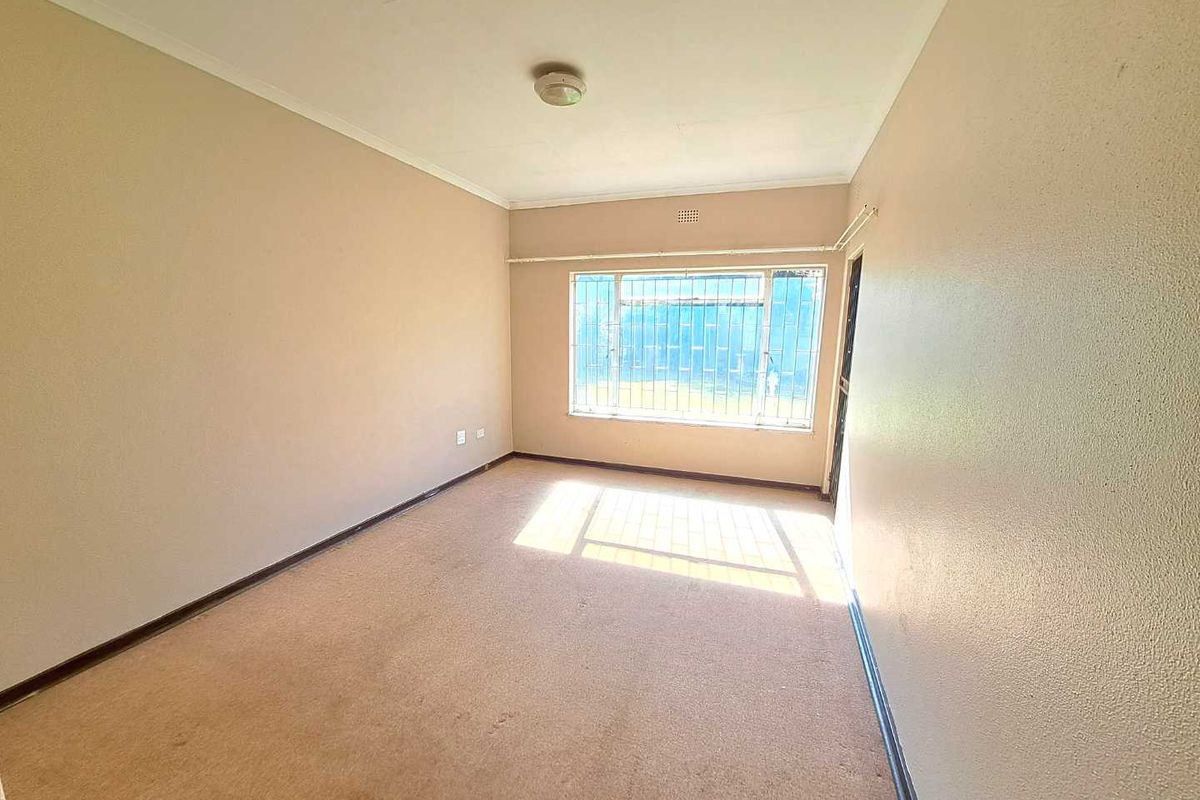 An empty bedroom featuring carpeted flooring, a large window with security bars, and neutral wall finishes, ready for personalization.