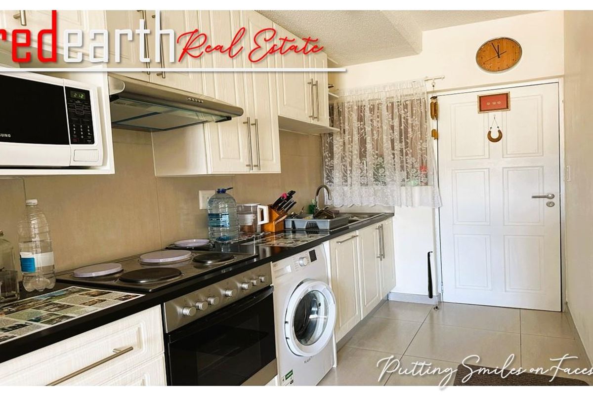 A functional kitchen featuring white cabinetry, a built-in oven with electric hob, extractor fan, and integrated laundry appliance space.