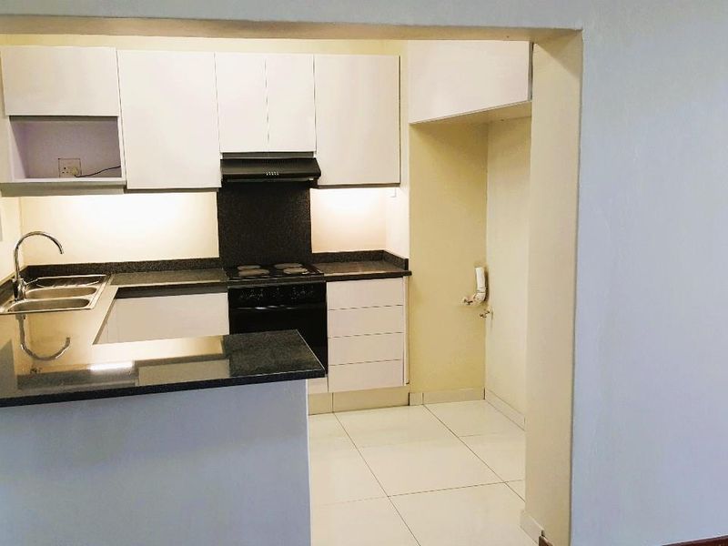 A clean, modern kitchen featuring white cabinetry, dark granite countertops, integrated stove and extractor fan, and tiled flooring.