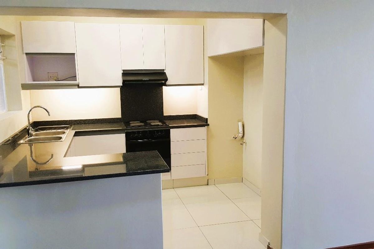 A clean, modern kitchen featuring white cabinetry, dark granite countertops, integrated stove and extractor fan, and tiled flooring.