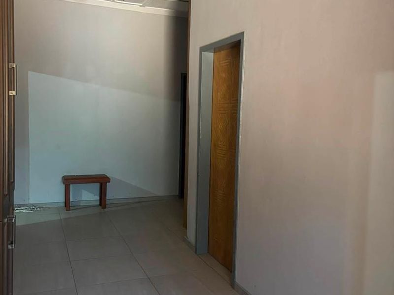 A vacant hallway featuring tiled flooring, a wooden door, and a ceiling access hatch, requiring minor cosmetic repairs to the ceiling.