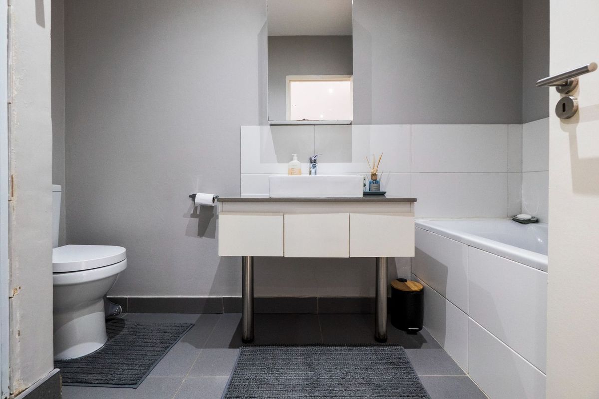 A modern bathroom featuring a wall-mounted vanity with a vessel sink, a bathtub with tiled surround, and a standard toilet.
