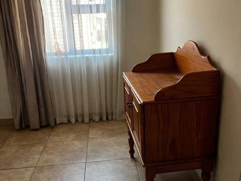 A bedroom featuring neutral tiled flooring and a window with curtain treatments, offering a clean and functional space.