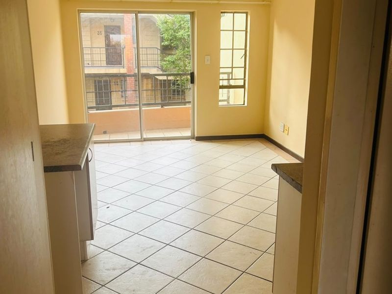 An empty open-plan living area featuring tiled flooring, kitchen cabinetry with laminate countertops, and access to a balcony through a sliding glass door.
