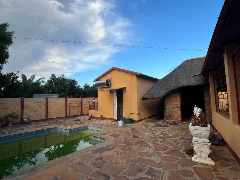 Outdoor pool area featuring stone paving, a thatched roof structure, and a perimeter wall, requiring maintenance to the pool and surrounding surfaces.