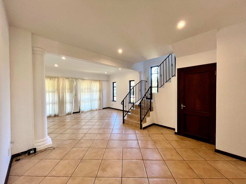 Spacious open-plan living area featuring tiled flooring, a decorative column, and a staircase with a metal railing.