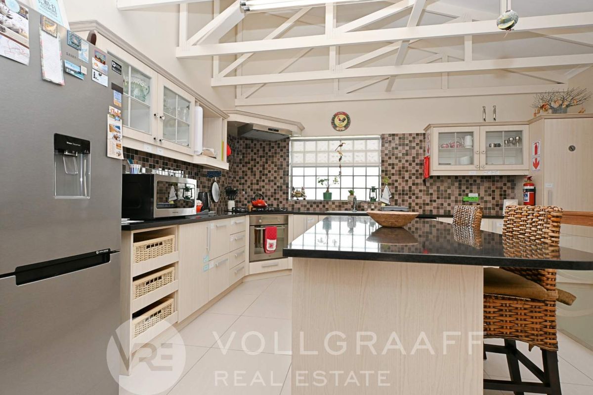 Spacious kitchen featuring a central island, granite countertops, built-in oven, extractor fan, and distinctive exposed roof trusses for an airy feel.