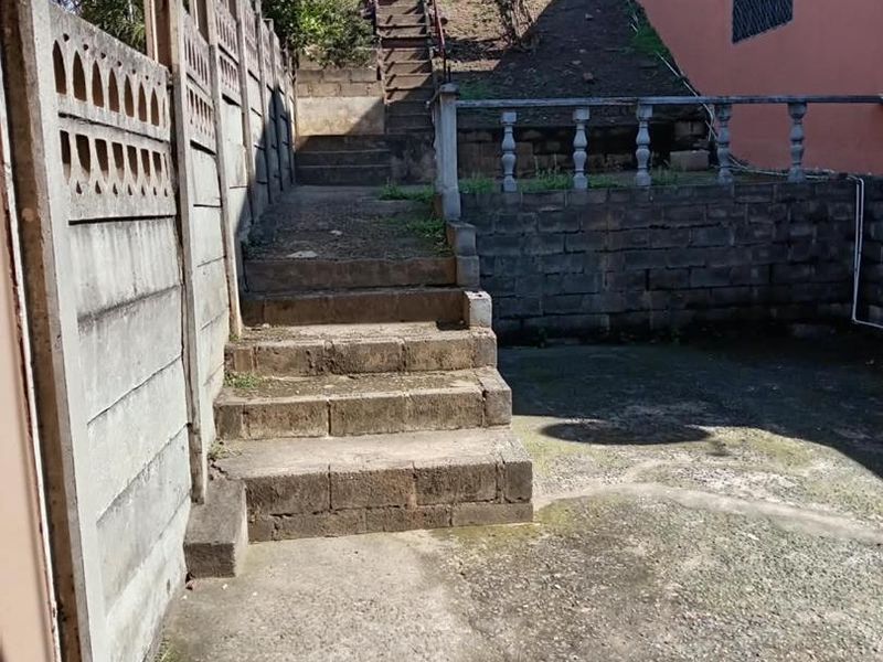 Rear exterior area featuring a concrete staircase, retaining wall, and precast boundary wall, showing significant signs of weathering and wear.