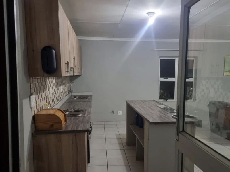 A functional kitchen featuring light wood-tone cabinetry, laminate countertops, a central island, and tiled flooring, offering a clean and practical workspace.