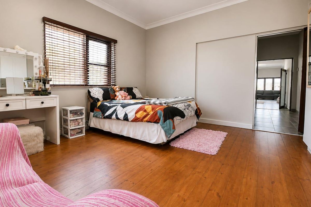 A well-maintained bedroom featuring warm timber flooring, a built-in wardrobe, and natural light through venetian blinds.