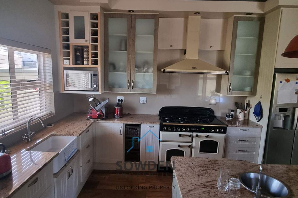 A well-appointed kitchen featuring granite countertops, a farmhouse-style sink, built-in cabinetry, a gas range with extractor hood, and a central island with a prep sink.