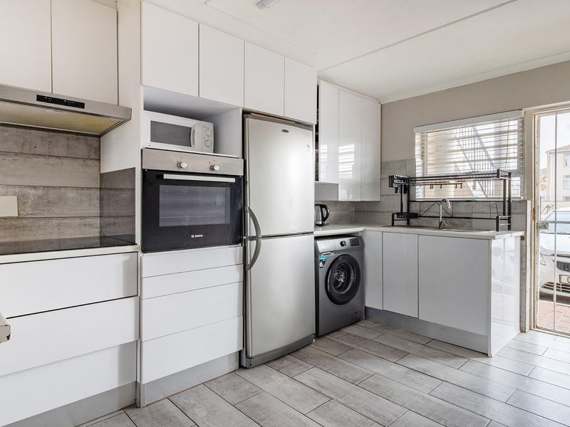 Modern kitchen featuring white cabinetry, built-in oven, extractor fan, tiled backsplash, and direct access to an exterior area through a security gate.