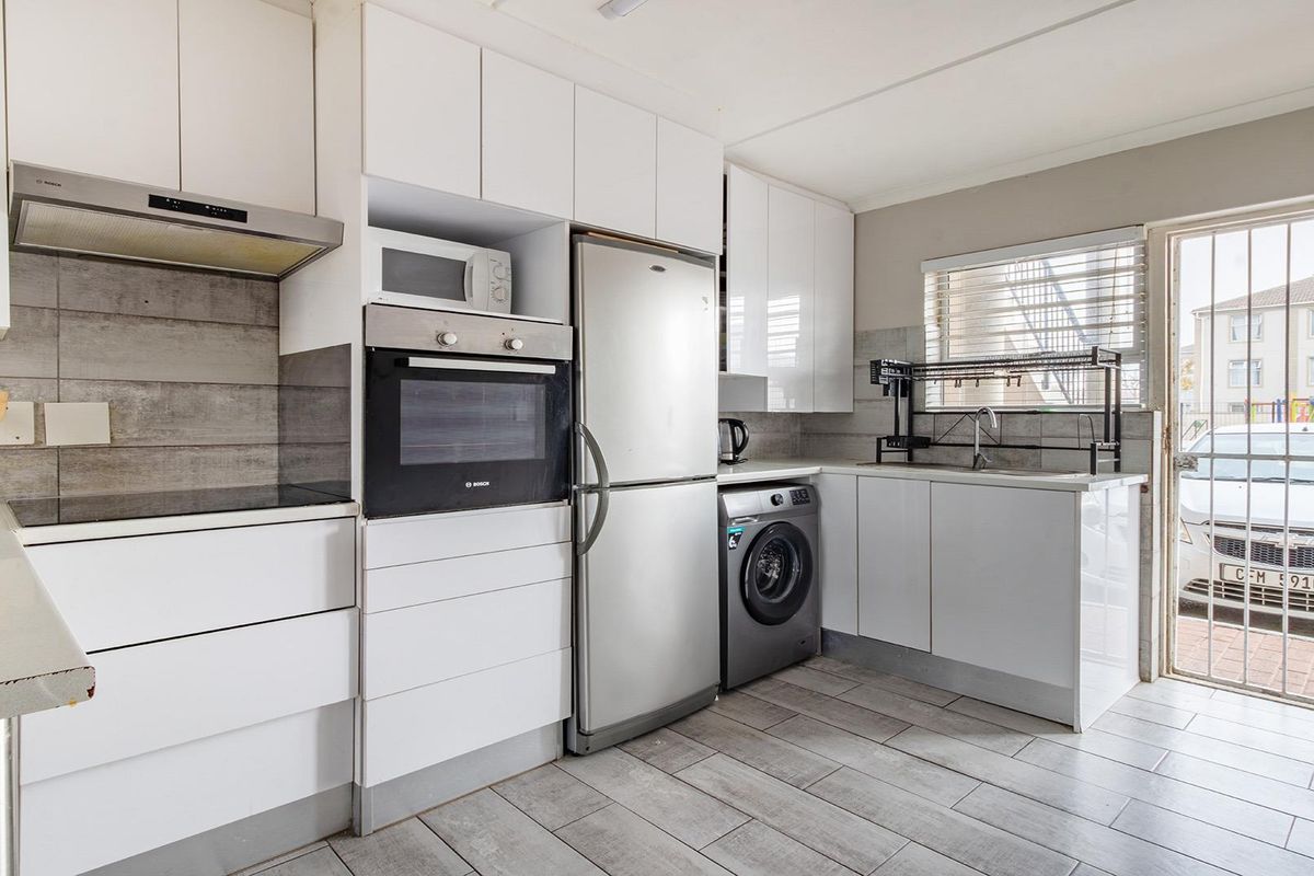 Modern kitchen featuring white cabinetry, built-in oven, extractor fan, tiled backsplash, and direct access to an exterior area through a security gate.