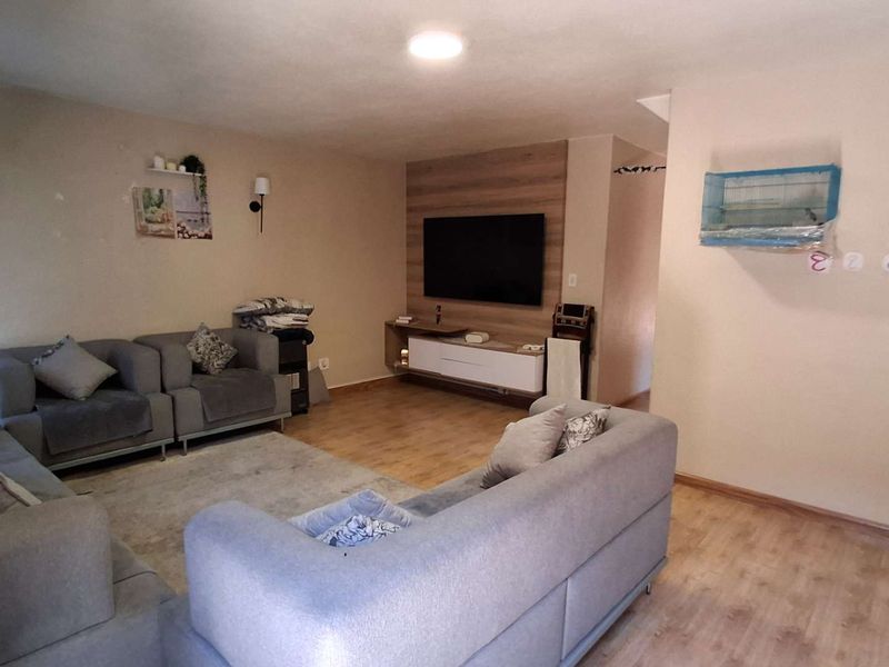 A spacious living room featuring laminate flooring and a modern built-in media wall unit, providing a functional and comfortable lounge area.