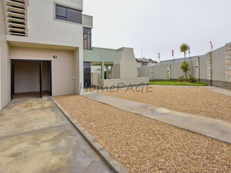 Rear exterior view featuring a concrete patio, gravel landscaping, and a built-in outdoor fireplace against a modern multi-story residential structure.
