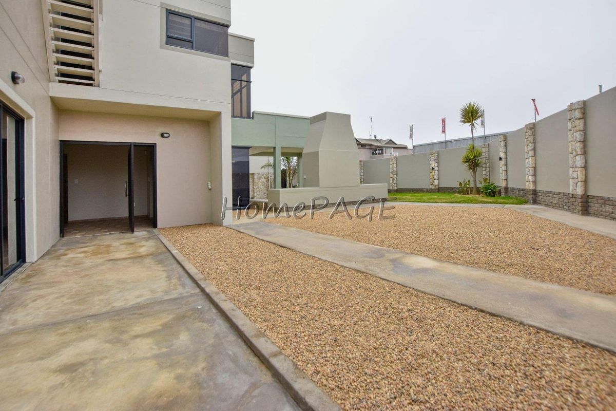 Rear exterior view featuring a concrete patio, gravel landscaping, and a built-in outdoor fireplace against a modern multi-story residential structure.
