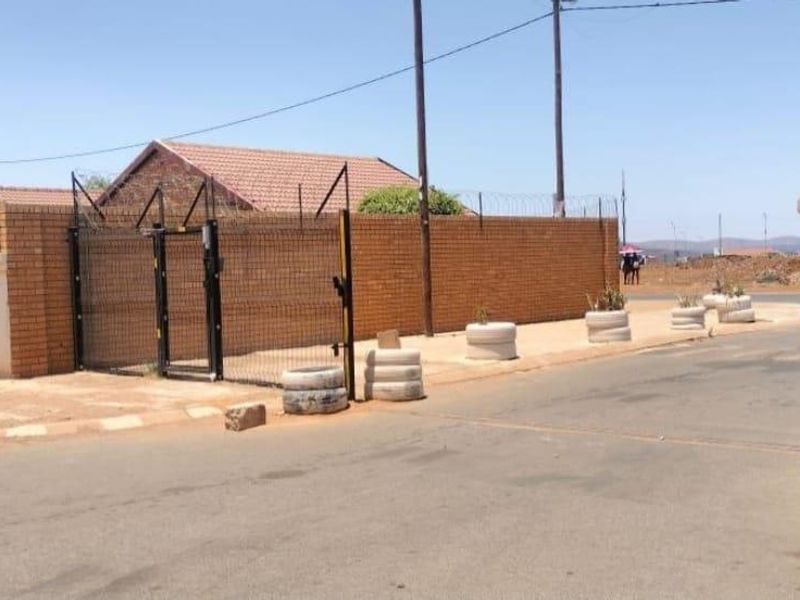 Street view of the property entrance featuring a brick boundary wall, security fencing with razor wire, and a metal gate.