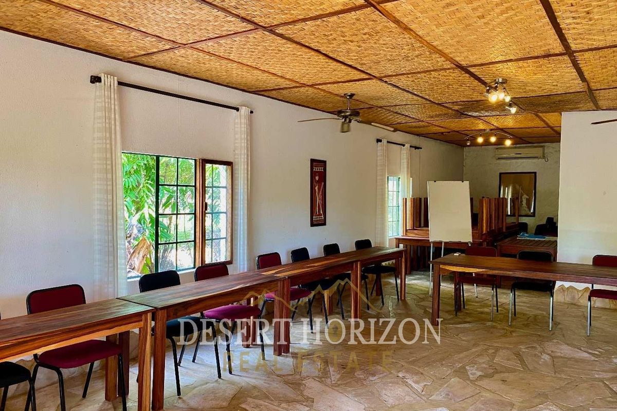 A spacious lodge function room featuring a woven bamboo ceiling, stone flooring, and large windows providing natural light.