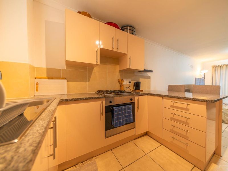 Open-plan kitchen featuring light-toned cabinetry, granite countertops, built-in oven, gas hob, and tiled flooring, seamlessly flowing into the adjacent living area.