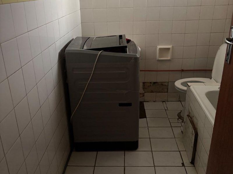 A dated bathroom featuring ceramic tiling, a bathtub, and a toilet, currently showing signs of wear and requiring maintenance or renovation.
