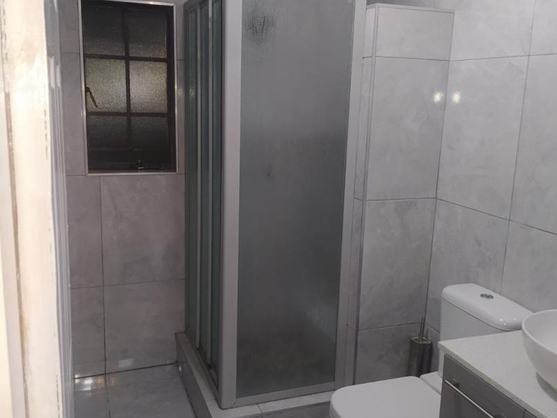 A modern bathroom featuring a glass shower enclosure, a sleek vanity with a basin, and neutral grey floor-to-ceiling wall tiles.