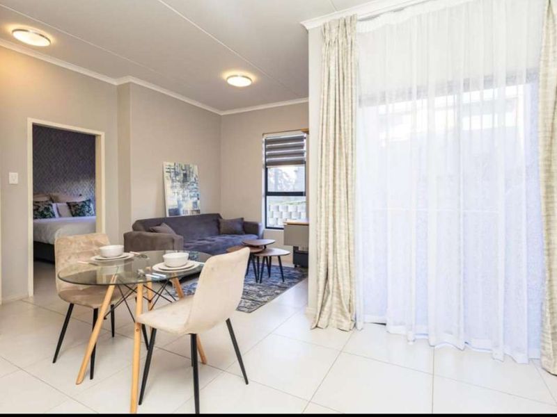 Bright open-plan living and dining area featuring neutral tiled flooring, recessed lighting, and large sliding glass doors leading to an outdoor space.