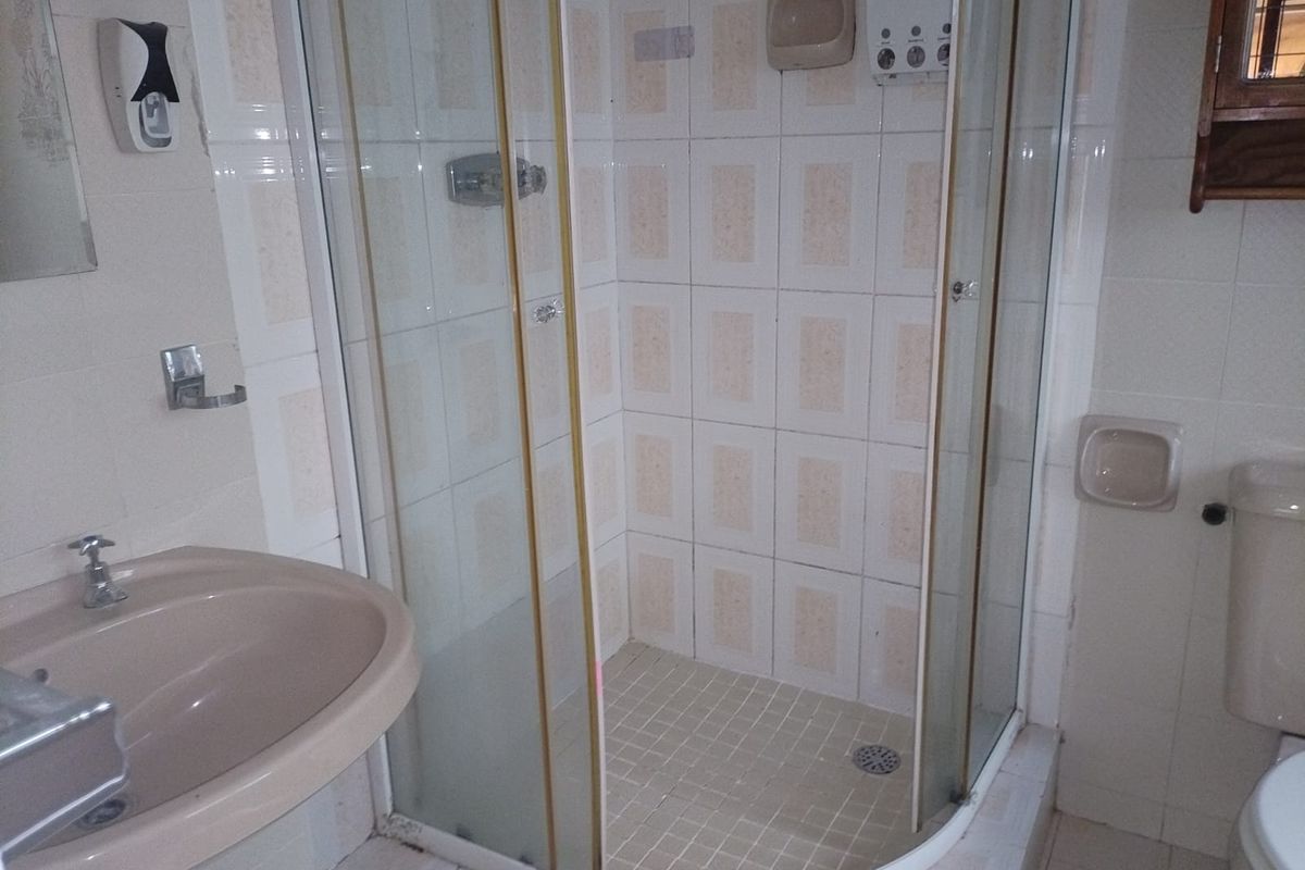 A functional bathroom featuring a corner shower enclosure, pedestal basin, and toilet with dated wall and floor tiling.