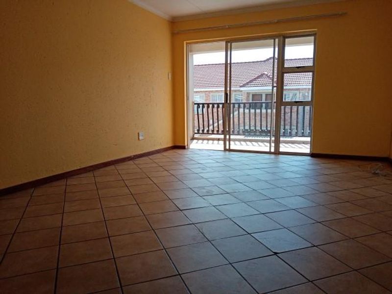 An empty living room featuring ceramic tiled flooring and a sliding glass door providing access to a balcony.