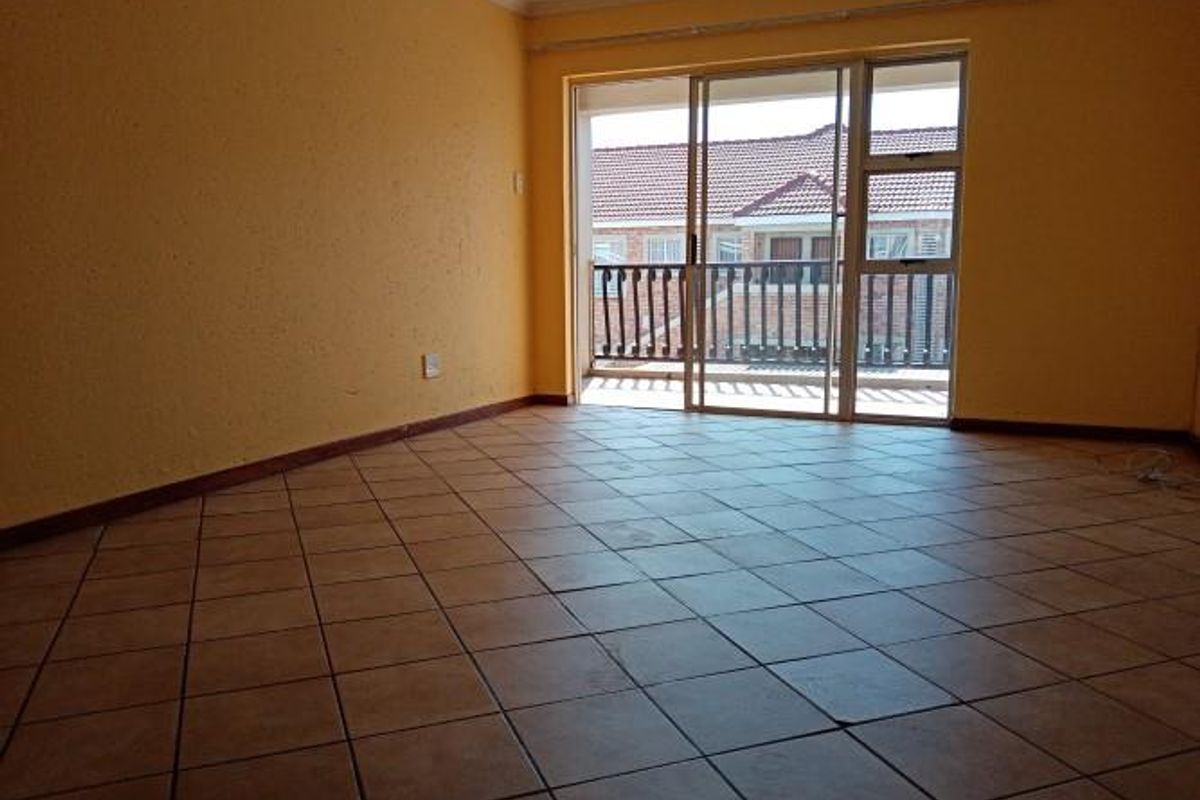 An empty living room featuring ceramic tiled flooring and a sliding glass door providing access to a balcony.