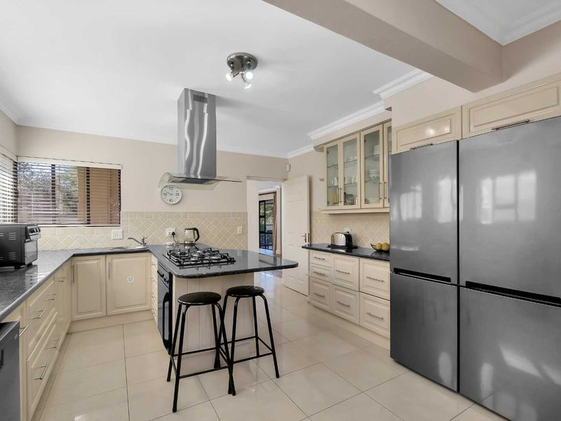 A well-appointed kitchen featuring granite countertops, a central island with a gas cooktop, stainless steel extractor fan, and ample built-in cabinetry.