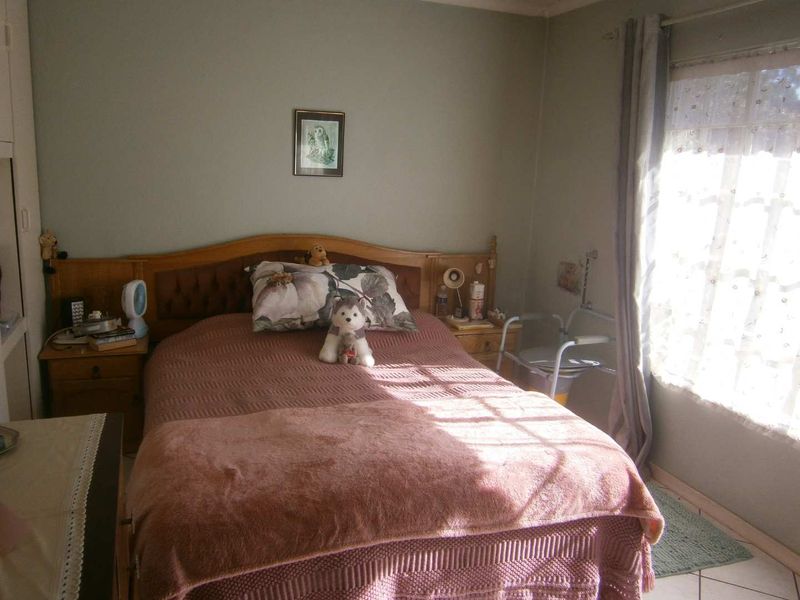 A functional bedroom featuring tiled flooring, a built-in wardrobe, and natural light through a window with curtain rails.