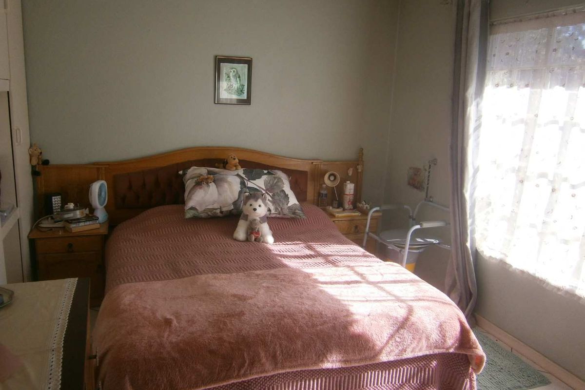 A functional bedroom featuring tiled flooring, a built-in wardrobe, and natural light through a window with curtain rails.