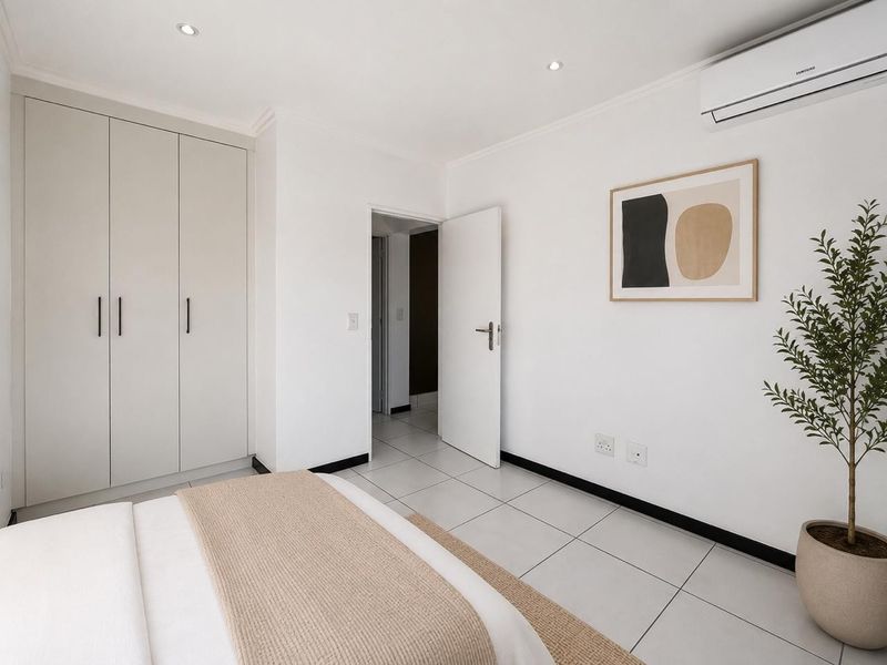 A bright, modern bedroom featuring neutral tiled flooring, built-in cabinetry, and a wall-mounted air conditioning unit.