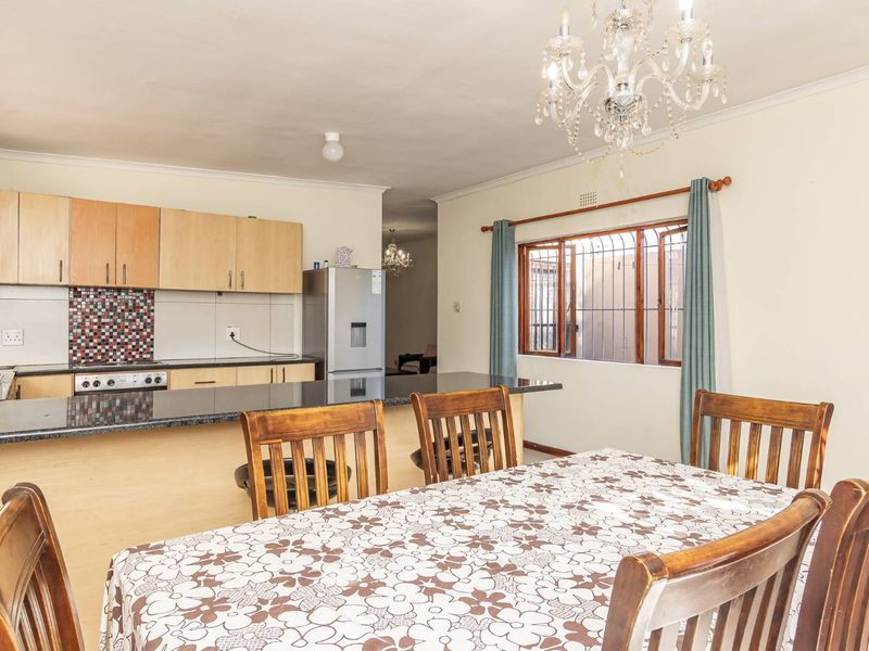 Open-plan kitchen and dining area featuring light wood cabinetry, granite countertops, tiled backsplash, and a classic chandelier, providing a functional and connected living space.