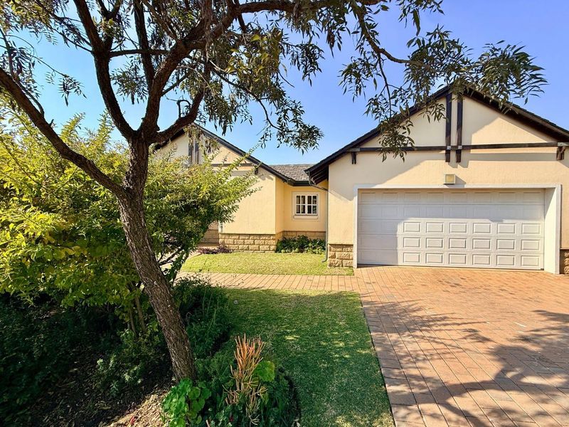 Front elevation of a well-maintained house featuring a paved driveway, double garage, and established garden with stone-clad exterior detailing.