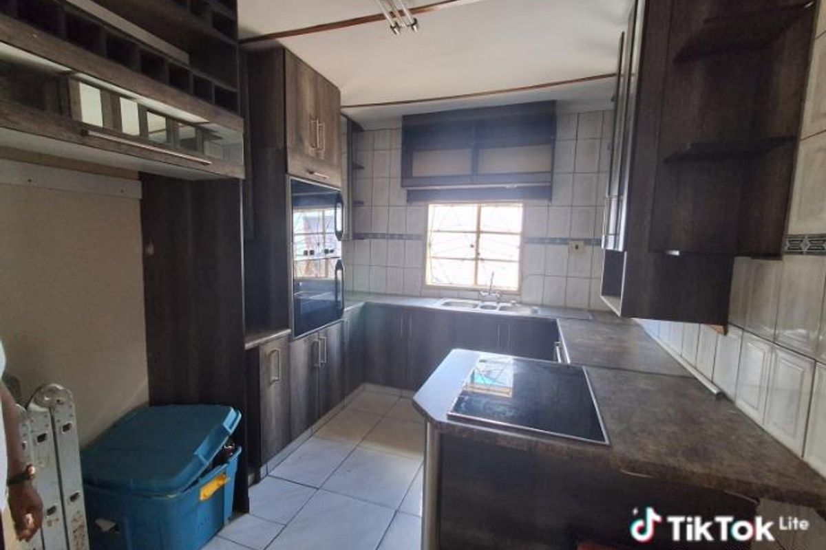 A functional kitchen featuring dark wood-toned cabinetry, built-in oven, integrated hob, and tiled splashbacks with a window overlooking the exterior.