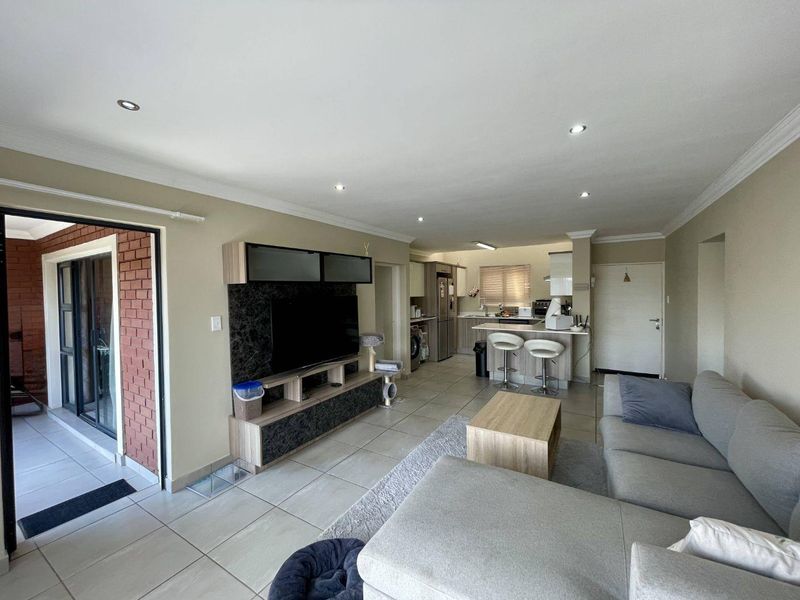 An open-plan living and kitchen area featuring tiled flooring, recessed lighting, a built-in media unit, and a breakfast bar connecting to the kitchen.