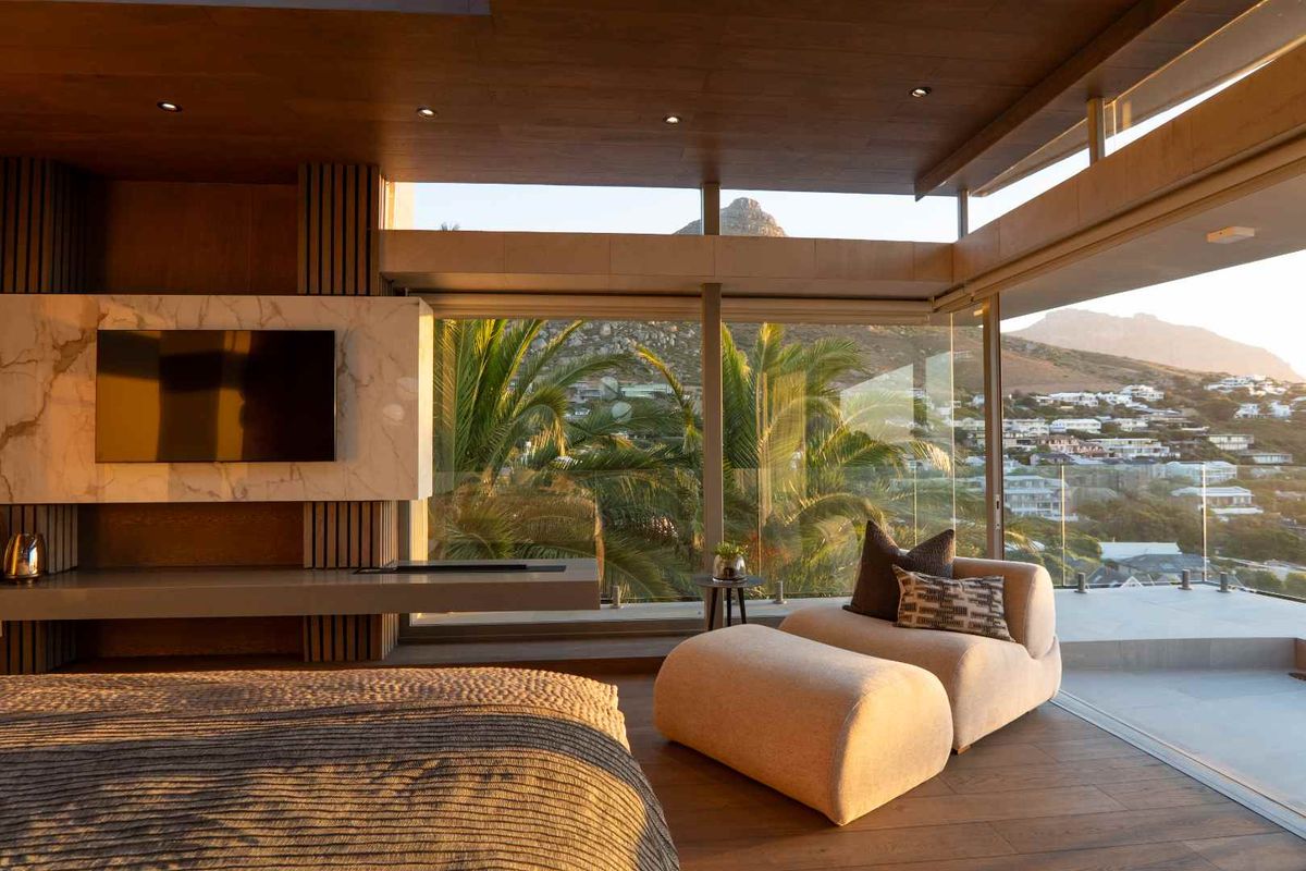 A luxurious bedroom featuring floor-to-ceiling glass walls, wood-paneled ceilings, marble feature wall, and expansive mountain and coastal views.