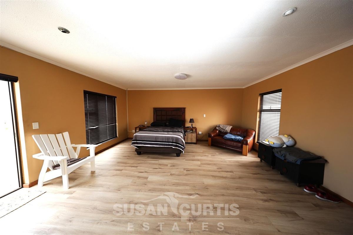 Spacious bedroom featuring light wood-look laminate flooring, recessed ceiling lighting, and large windows with fitted blinds, offering a bright and open living space.