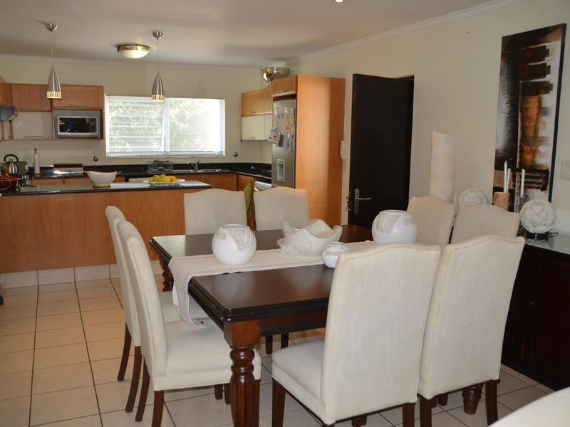 Open-plan dining area and kitchen featuring light wood cabinetry, granite countertops, and tiled flooring, creating a functional and connected living space.